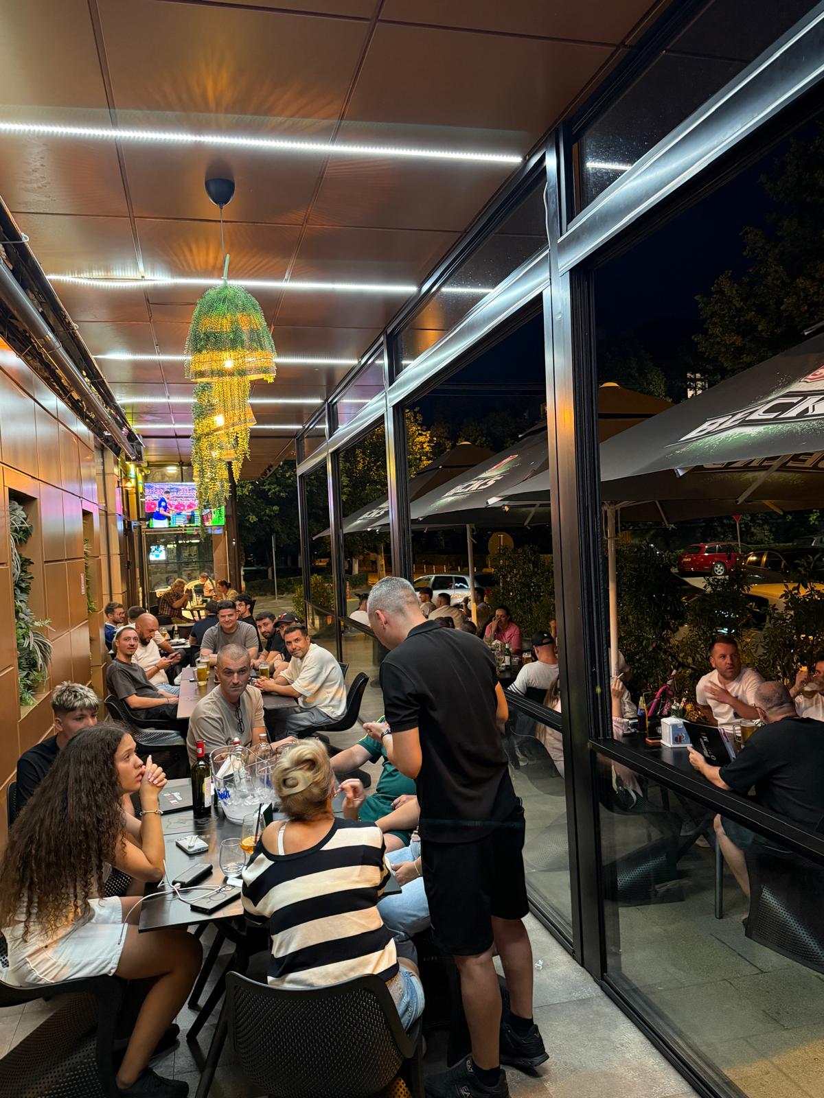 Oaspeți serviți la mese pe terasa acoperită a Trattoria Bona Mi